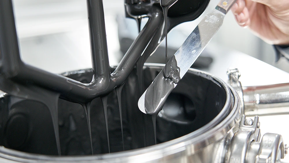 Engineer sampling battery electrode slurry from a planetary mixer during pilot line validation